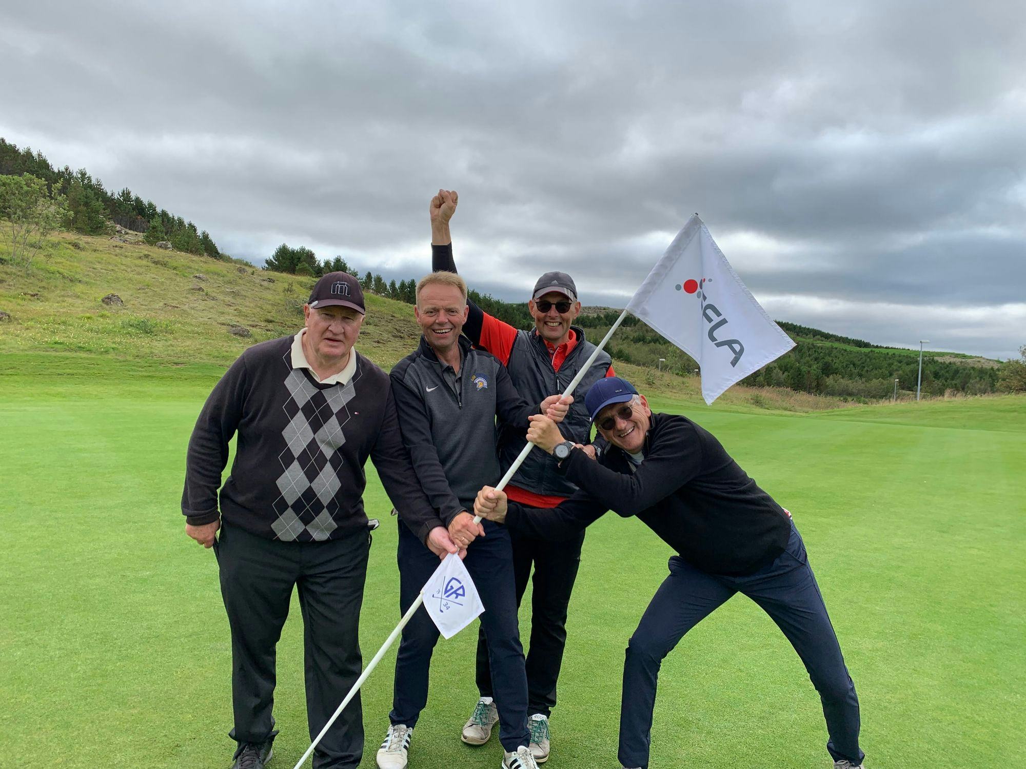 Four men posing joyfully on a golf course with one of them holding a flagstick